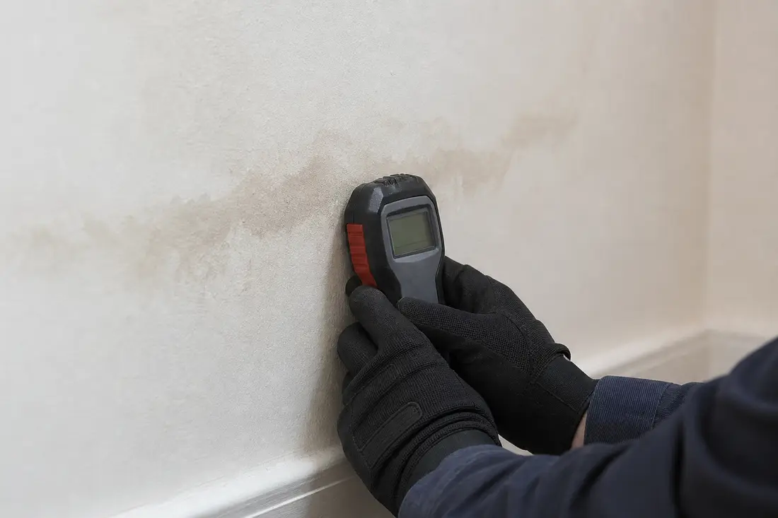 Sanitärinstallateur misst mit einem Feuchtigkeitsmessgerät die Wand neben einem vermuteten Wasserleck